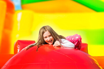 Happy smiling little girl having lots of fun on a inflate yellow castle while jumping on big balls.