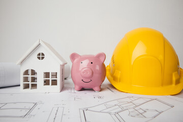 Yellow helmet, piggy bank and model of house on drawings