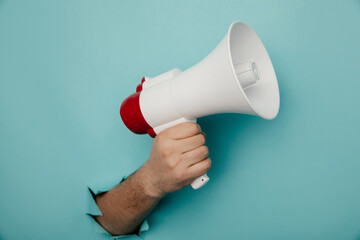Man's hand arm hold megaphone isolated through torn blue paper