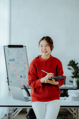 Charming Asian woman with a smile standing holding papers and mobile phone at the office.