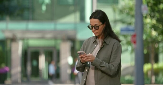 Attractive caucasian young woman with dark hair standing on the street, chatting and raising hand calling taxi, dressed in smart casual cloth 