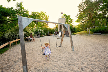 Baby girl swing in children's playground toy set in public park.