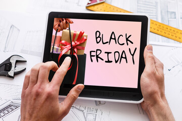 Black Friday sale concept. Tablet pad with sign Black Friday on screen, shopping bag, gift box over black background