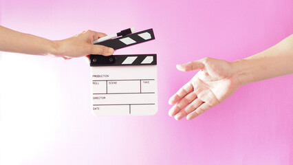 Hand is holding clapper board and marker pen and sending clapperboard to ather hand on pink background.