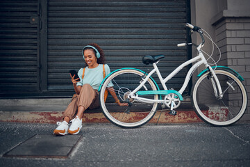 Bike, woman and headphone with phone in city relax, with bicycle and happy texting, social media apps and chat. Girl, lady and with eco friendly transportation, trendy or edgy look sit on sidewalk © Kay Abrahams/peopleimages.com