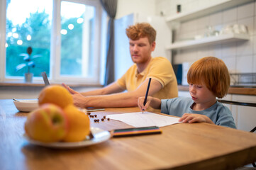 Obraz premium Cute little boy drawing while his dad working