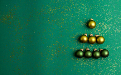 Alternative green and yellow christmas balls make tree on jade green background with gold colored glitter. Christmas Holidays and present concept flat lay with copy space