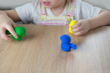 close-up plasticine toys in hands of toddler, small child, blonde girl 2 years old sculpts figures of characters from colored dough, concept of fine motor skills, tactile sensations, creativity