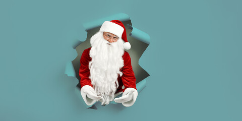 Emotianal Santa Clause spread arms in forward through paper hole. Advertisement concept