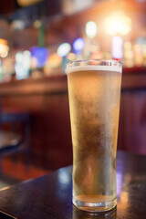 Pint glass of lager beer of cider on a table in bar in focus. Selective focus. Cinematic tone. Drinking after work concept. Enjoy cold craft alcohol drink in a traditional Irish pub. Vertical image.