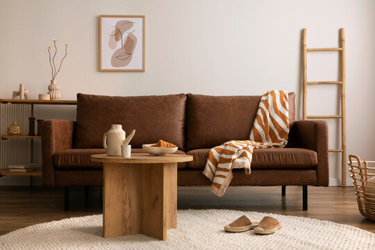 Warm and cozy interior of living room space with brown sofa, round beige carpet, wooden coffee table, mock up poster frames, decoration and elegant personal accessories. Cozy home decor. Template.	
