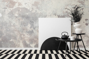 Interior design of loft industrial apartment with painting, black round coffee table, vase with dried leaves, patterned carpet. Grey concrete wall. Home decor. Template.