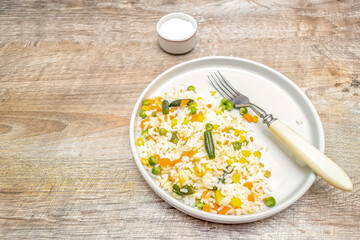 Risotto rice with vegetables and spices served on gray plate with fork. Rustic healthy lunch dinner food wooden background. top view, copy space