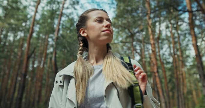 Selective focus young blonde girl with braids wearing sporty suit taking on travelled backpack with mat on starting her trip in forest looking into distance planning rout .