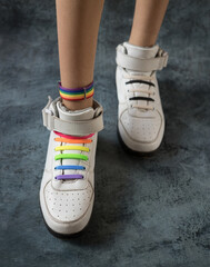Young unisex legs with a rainbow bracelet in white sneakers with rainbow color laces. Symbols of the LGBT community. A person has the right to change his life from black and white to rainbow 