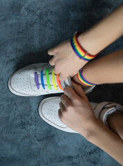 Young unisex legs with a rainbow bracelet in white sneakers with rainbow color laces. Symbols of the LGBT community. A person has the right to change his life from black and white to rainbow 