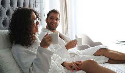 Couple in white bathrobe on a bed in a hotel. Morning in the hotel room.