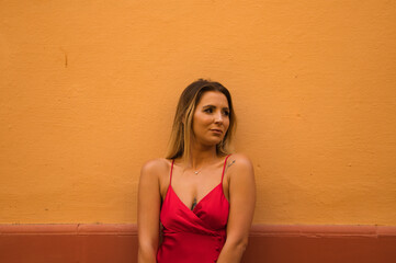 Young, blonde, beautiful woman in a red dress is visiting seville. The woman is posing for the camera very elegant for the photos. The woman has a yellow wall in the background. Holidays and travels.