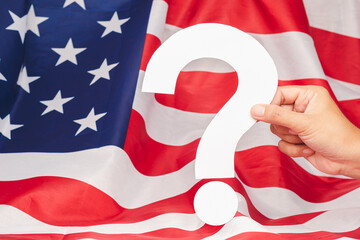 Hand holding a white question mark over the American flag