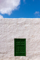 Rustic green wooden door in weathered white wall and blue sky
