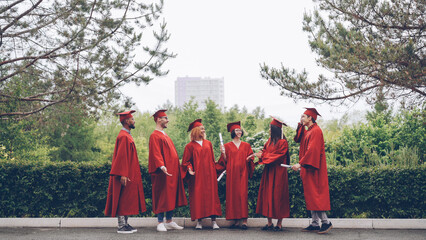 happy graduates laughing and celebrating graduation on college campus. Education, success and...