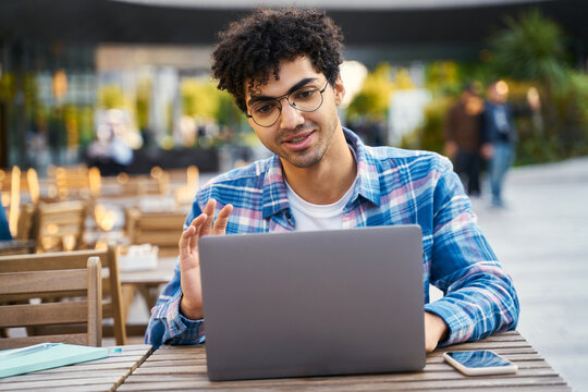 Middle Eastern Man Freelancer Using Laptop Computer Waving Hand, Having Video Call Sitting At Workplace. Smart Student Wearing Eyeglasses Studying, Online Education 