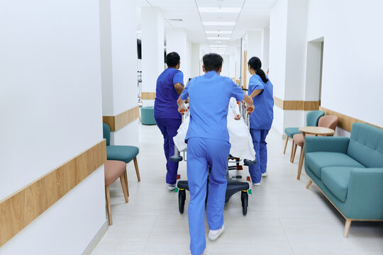 Hospital care team wheeling patient on medical gurney at emergency department of hospital, back view