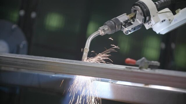 Footage of sparks falling off a steel frame while a robotic welder is working on it.