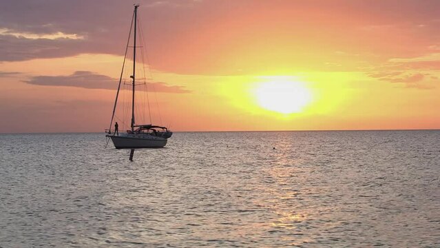 Sailboat anchored on Florida Coast with gorgeous creamsicle sunset. Boat passenger takes photo of sunset on calm waters.