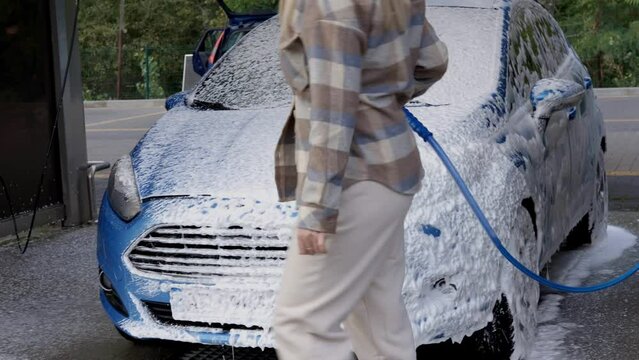 Woman washing a car in a self-service car wash station with wahing foam. Wash car self-service station