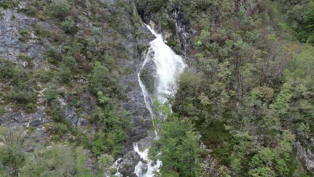 Waterfall cascading though trees Lake Bohinj Slovenia drone aerial push in shot
