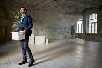 Portrait of young businessman walking out empty room with flower. Business closure. Depression and...