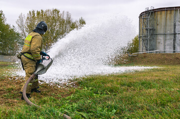 A firefighter in protective clothing extinguishes the fire by feeding foam. A firefighter...