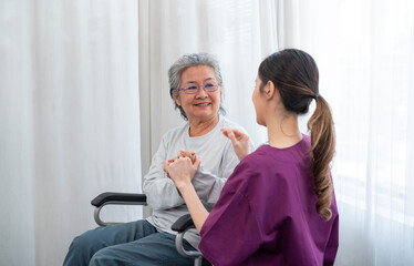 Asian young nurse taking care and talking mature female patient sitting on wheelchair in hospital. Healthcare concept.