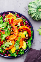 Healthy vegan eating, autumn pumpkin salad with baked honey pumpkin slices, lettuce, arugula, pomegranate seeds and walnuts. Comfort food. Top view