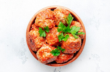 Meatballs in tomato sauce in wooden bowl on white kitchen table background, spices and herbs. Delicious home cooking. Top view