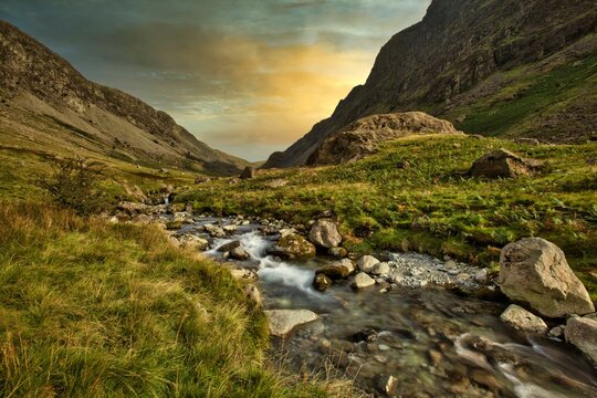 Scenic view of waterfall to the rocky river under green mountains in the forest under sunset