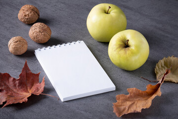 Mockup autumn composition of dry leaves, apples and walnuts. White notepad with blank sheets for text. Selective focus.