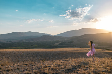 Naklejka na ściany i meble a girl in a pink dress walks across the field against the backdrop of mountains.