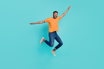 Fototapeta na wymiar Full length photo of impressed funny guy wear orange t-shirt jumping high arms sides isolated teal color background
