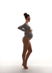 Full length portrait of a beautiful young pregnant woman dressed in a knitted bodysuit on a white background. Happy motherhood. Waiting for a baby.
