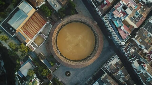 Aerial top  down view of round Spanish coliseum &ndash; circus arena building for theatre, sports, gladiators fight, racing and etc. Camera is rising above the coliseum and city center with rooftops.