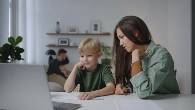 Mom and son are looking at the laptop screen analyzing lessons with distance learning. Learn foreign languages and learn math together. The concept of motherhood