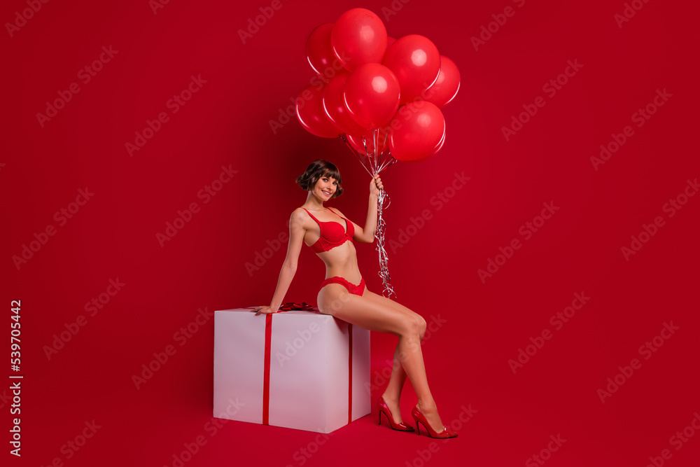 Canvas Prints Full length body size view of fit chic cheery girl sitting on big giftbox holding festal balls isolated on shine red color background