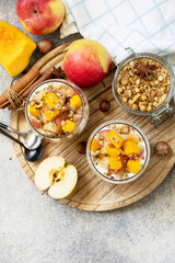 Healthy autumn or winter breakfast granola. Homemade dessert with yogurt, granola, caramel apples and pumpkin, cinnamon, nuts on a stone table. View from above. Copy space.