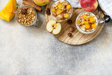 Healthy autumn or winter breakfast granola. Homemade dessert with yogurt, granola, caramel apples and pumpkin, cinnamon, nuts on a stone table. View from above. Copy space.