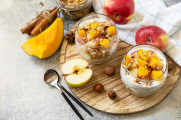 Healthy autumn or winter breakfast granola. Homemade dessert with yogurt, granola, caramel apples and pumpkin, cinnamon, nuts on a stone table. Copy space.