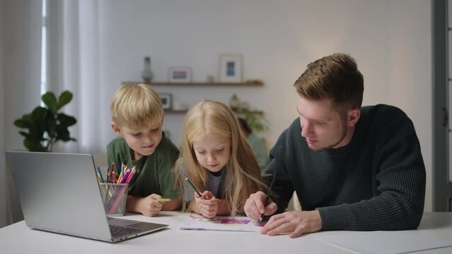 The general plan: A boy and a girl together with their dad do homework and paint a drawing with pencils. Home schooling. remote education tutoring. Caring father with children