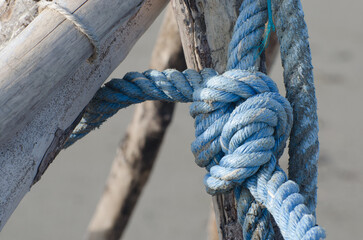 Dettaglio di una corda azzurra annodata e legata ad una struttura di legno sulla spiaggia di...
