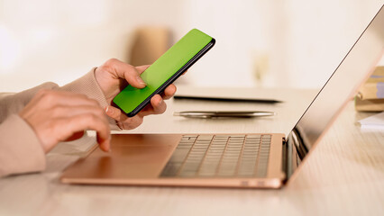 Cropped view of freelancer using smartphone and laptop with blank screen at home.